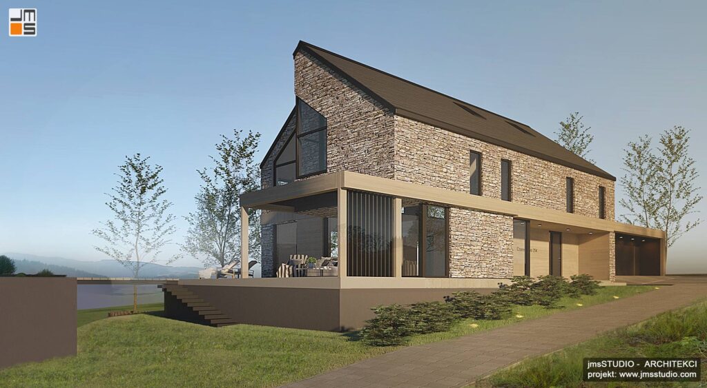 Lekkie nadwieszenie bryły budynku tworzy zadaszenie tarasu w projekcie domu z kamienną elewacją pod Krakowem na działce ze spadkiem