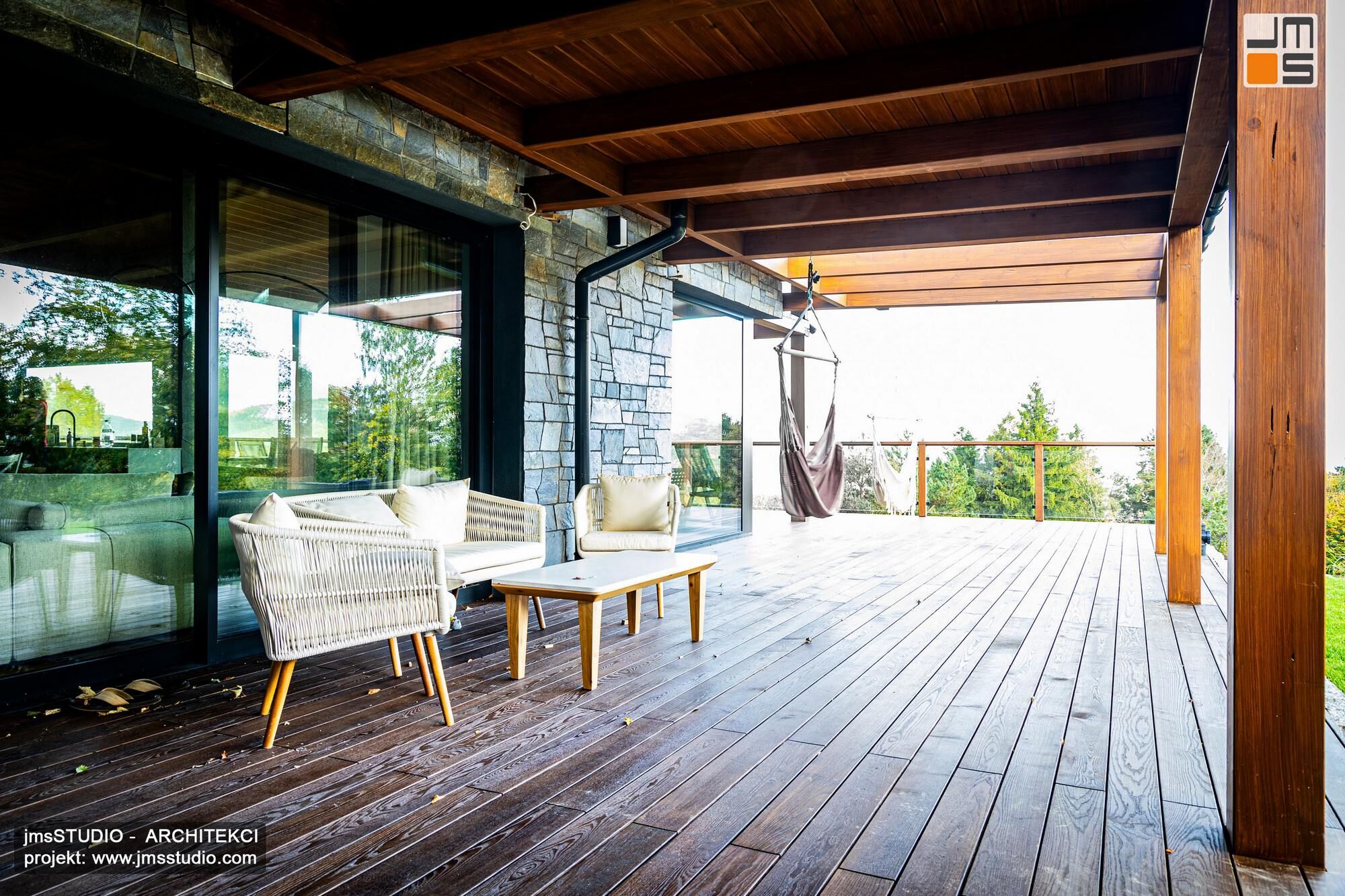 duży zadaszony drewniany  taras świetnie koresponduje z szarą kamienną elewacją i antracytową stolarką aluminiową w nowoczesnym projekcie rezydencji w górach