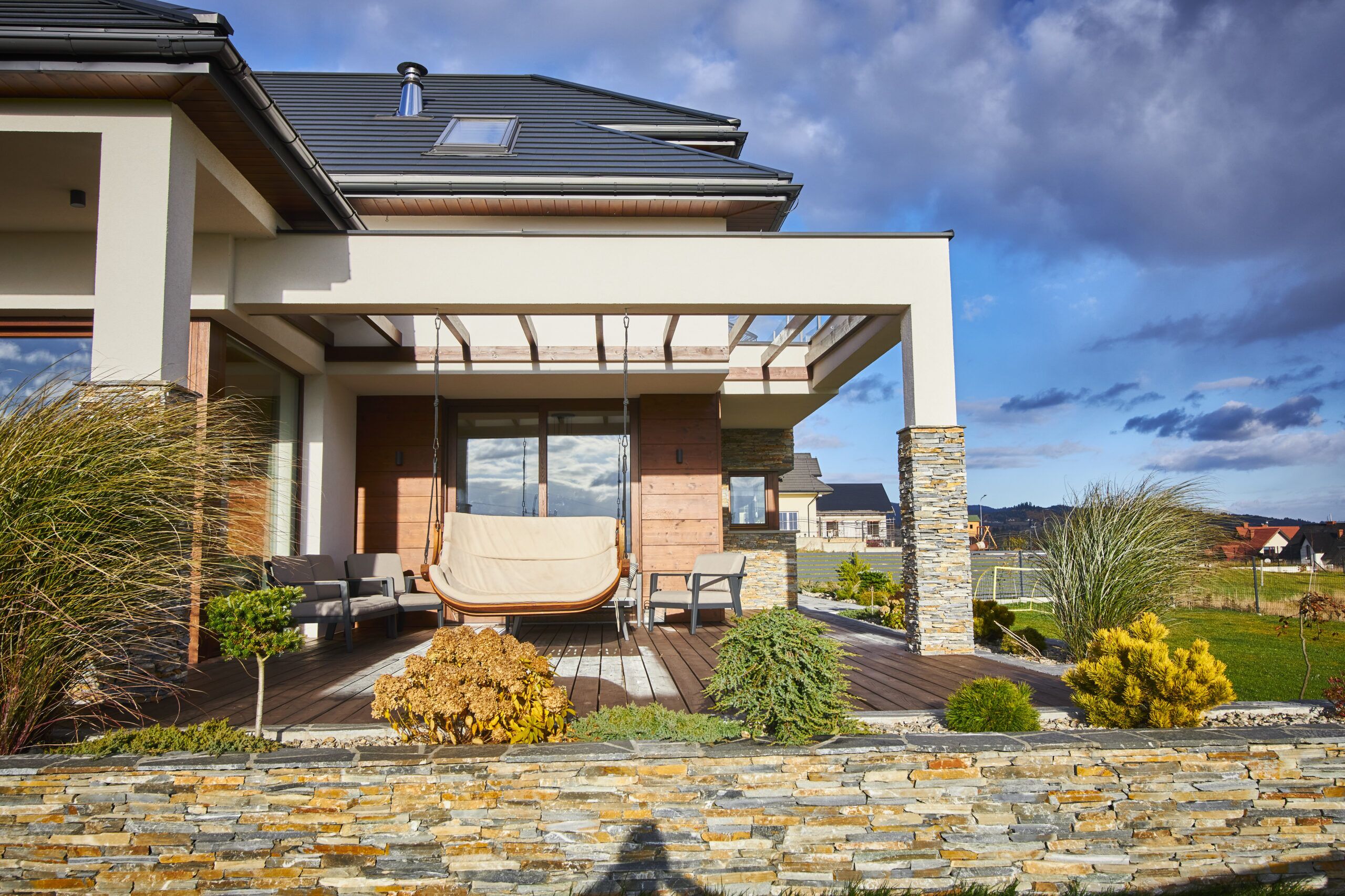 kamienna podmurówka z łupka i pergola to pomysł na piękną elewacje ogrodową z dużymi oknami w nowoczesnym domu dużej rezydencji w Nowym Sączu