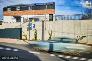 Mur oporowy z betonu architektonicznego jest również ścianą garażu podziemnego w projekcie nowoczesnego domu rezydencji miejskiej na działce ze spadkiem z detalem z cegły klinkierowej na elewacji