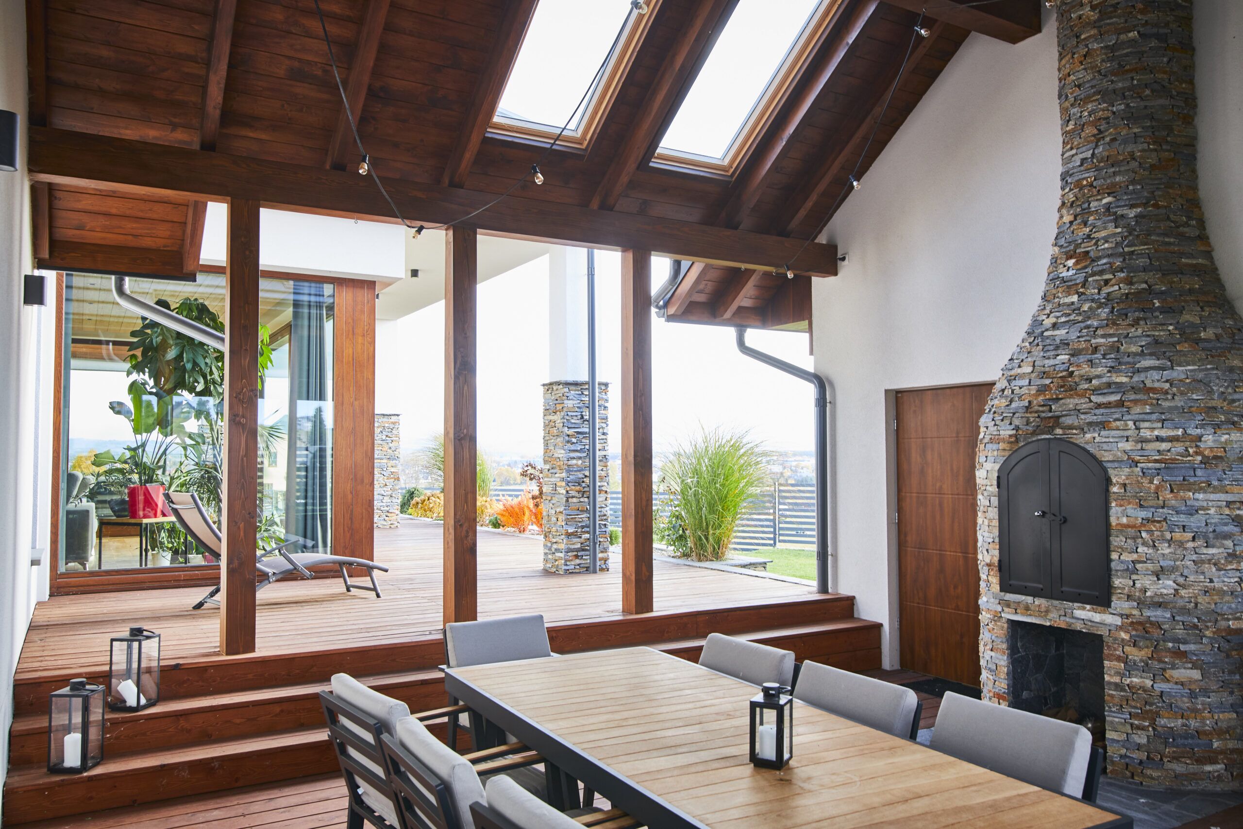 Projekt dużego domu w Nowym Sączu obejmuje przestrzeń gilową pod zadaszeniem wiatą z piecem opalanym drewnem z kamienia łupek z drewnianą podłogą